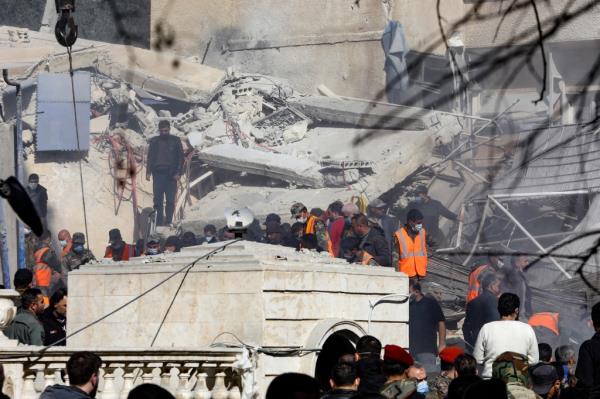 Civilians and rescuers wearing orange vests gather around a destroyed building in Damascus.